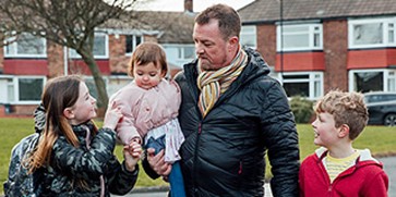 father with baby and two older children outside of block of flats